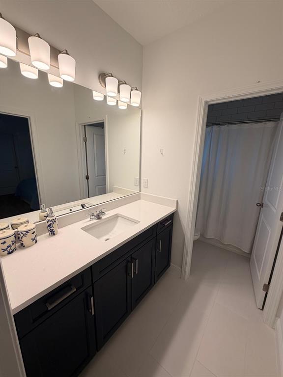 A bathroom features a dark vanity with a white countertop, a mirror, and overhead lighting — 1656 PYRAMID HILL STREET, MINNEOLA, FL