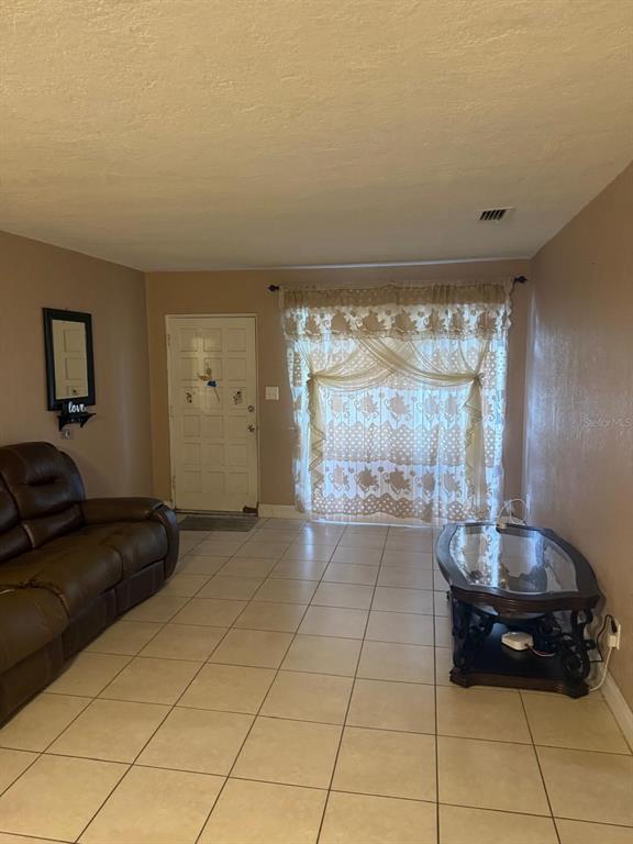A living room features beige tile flooring, a brown leather sofa, and a glass-topped coffee table — 1827 HEATHER AVENUE, TAMPA, FL