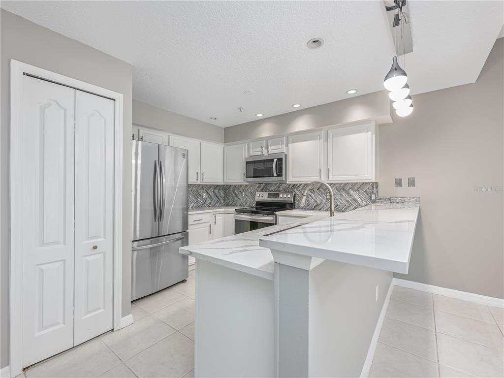 A kitchen features white cabinets, stainless steel appliances, a marble-look countertop, and a herringbone backsplash — 673 SANDY NECK LANE UNIT 103, ALTAMONTE SPRINGS, FL