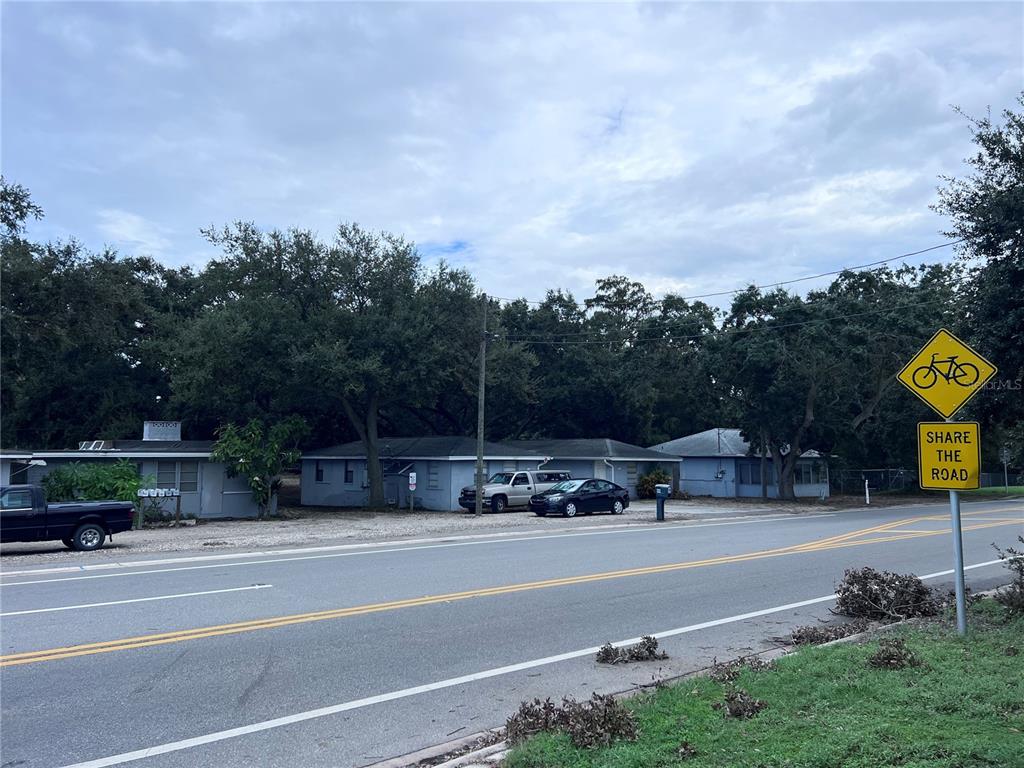 A street view shows a single-story residential building with a gravel parking area and trees — 1302 SUNSET PT RD, CLEARWATER, FL