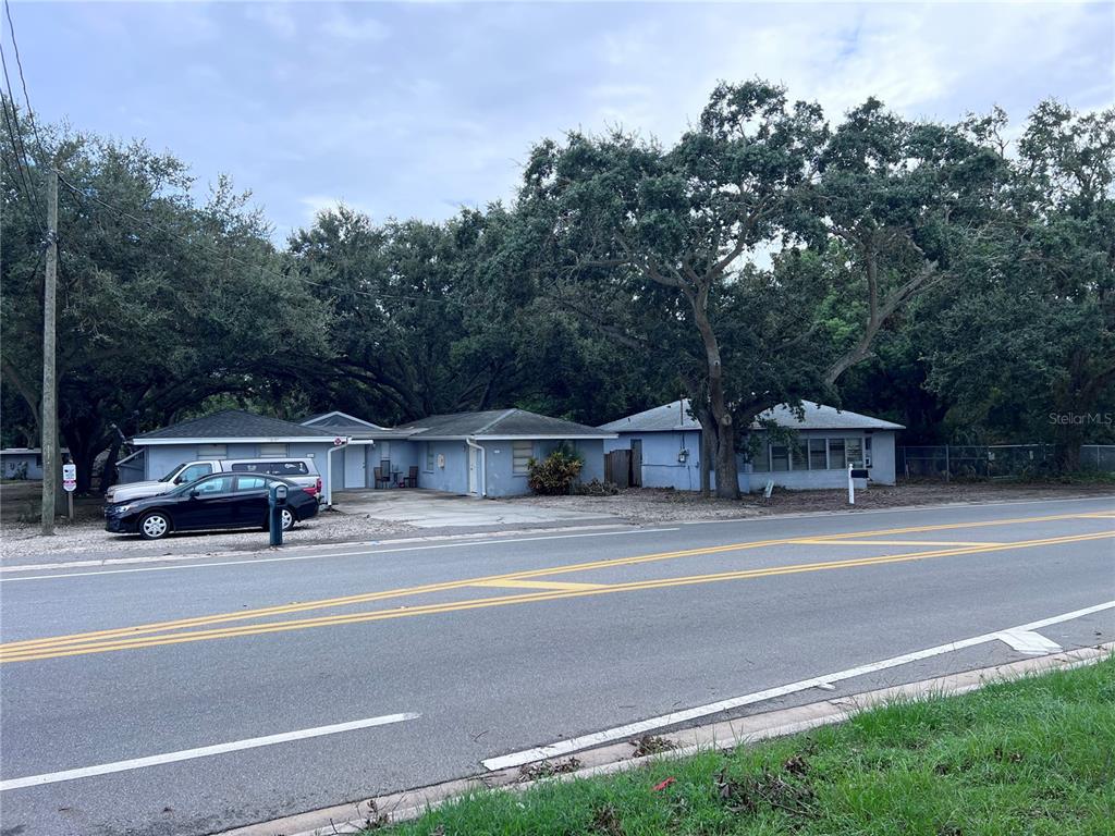 A single-story light blue house sits behind a paved road with large trees overhead — 1302 SUNSET PT RD, CLEARWATER, FL