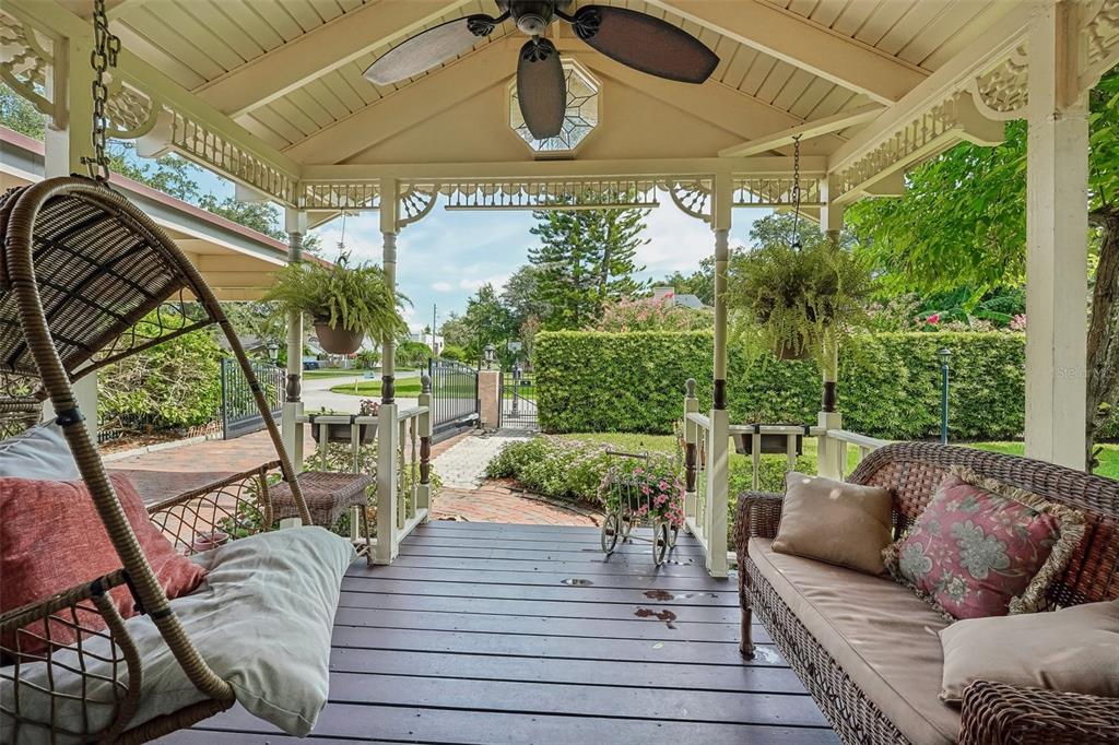 A covered wooden porch features a hanging chair, a wicker sofa, and a ceiling fan — 1020 VENETIAN AVENUE, ORLANDO, FL
