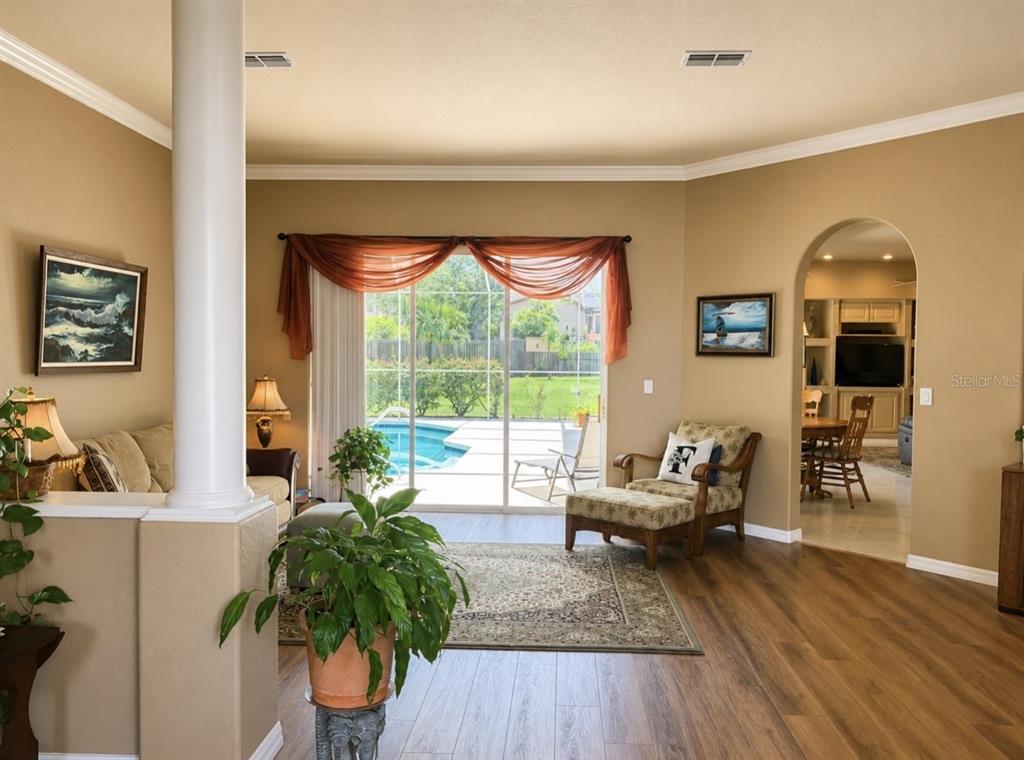 A living room with wood-look flooring, a white column, and sliding doors overlooking a pool — 7552 RIVER COUNTRY DRIVE, WEEKI WACHEE, FL