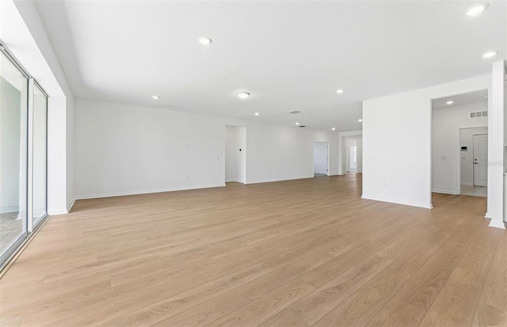 A spacious, empty room with light wood-look flooring, white walls, and large sliding glass doors — 9738 AUTUMN RIDGE AVENUE, RIVERVIEW, FL
