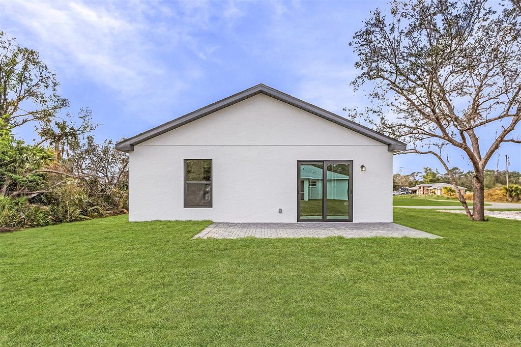 The back exterior of a white house features a paved patio, window, and sliding door — 3418 EAGLE PASS STREET, NORTH PORT, FL