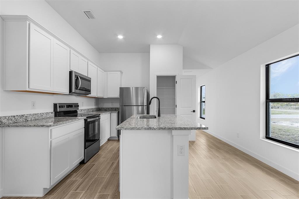 A modern kitchen features white cabinets, granite countertops, stainless steel appliances, and light wood flooring — 3418 EAGLE PASS STREET, NORTH PORT, FL