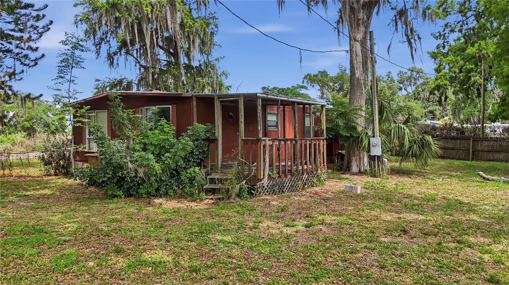 A weathered, brown mobile home with a front porch sits on a grassy, tree-filled lot — 4791 SUNSET ROAD, ST CLOUD, FL