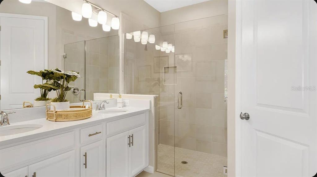 A bathroom features a double vanity with white cabinets, a glass-enclosed shower, and neutral tile — 5079 LOST KEY PLACE, ST CLOUD, FL
