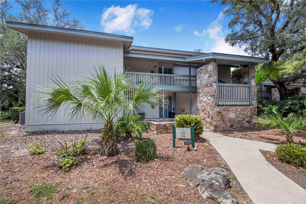 A two-story apartment building features light-colored siding, stone accents, and a palm tree in front — 816 PINEWOOD COURT UNIT 3126, HAINES CITY, FL