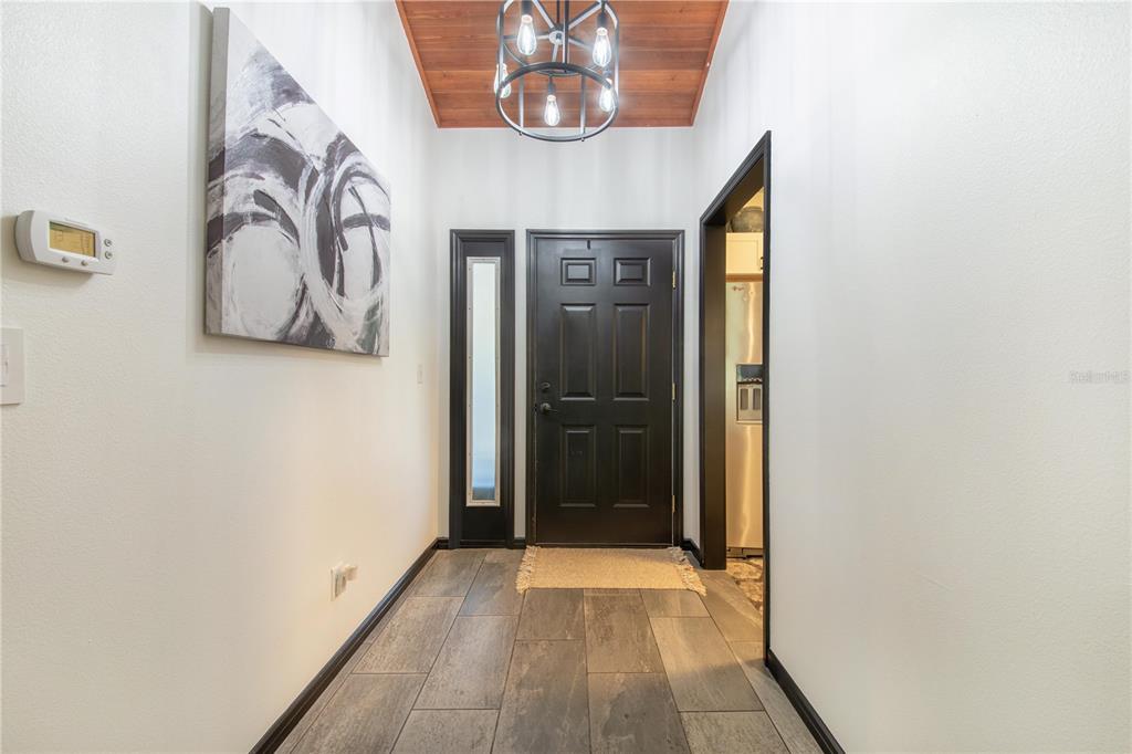 A foyer features a black front door, wood-paneled ceiling, chandelier, and gray tile flooring — 816 PINEWOOD COURT UNIT 3126, HAINES CITY, FL