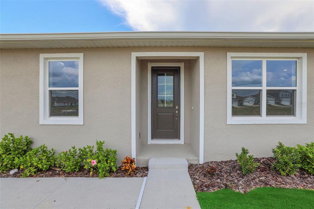 A tan stucco house exterior features a dark brown front door and two white-framed windows — 7551 SEA OAK COURT, PARRISH, FL