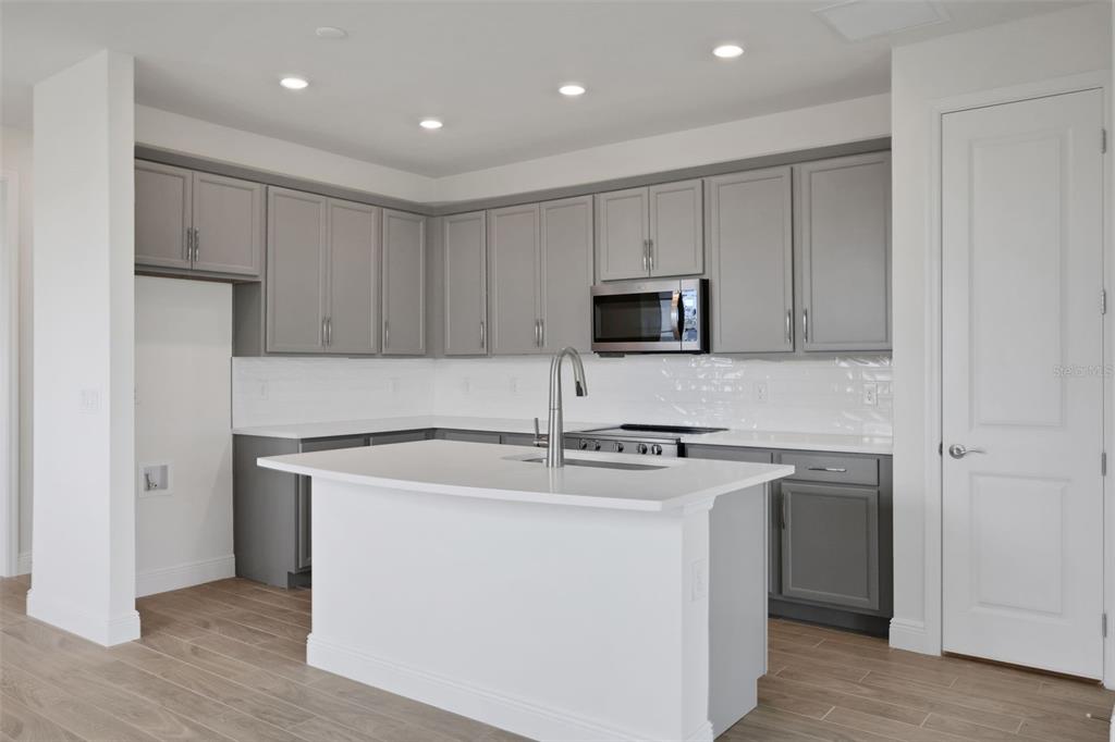 A modern kitchen features gray cabinets, white countertops, a central island, and light wood flooring — 7551 SEA OAK COURT, PARRISH, FL