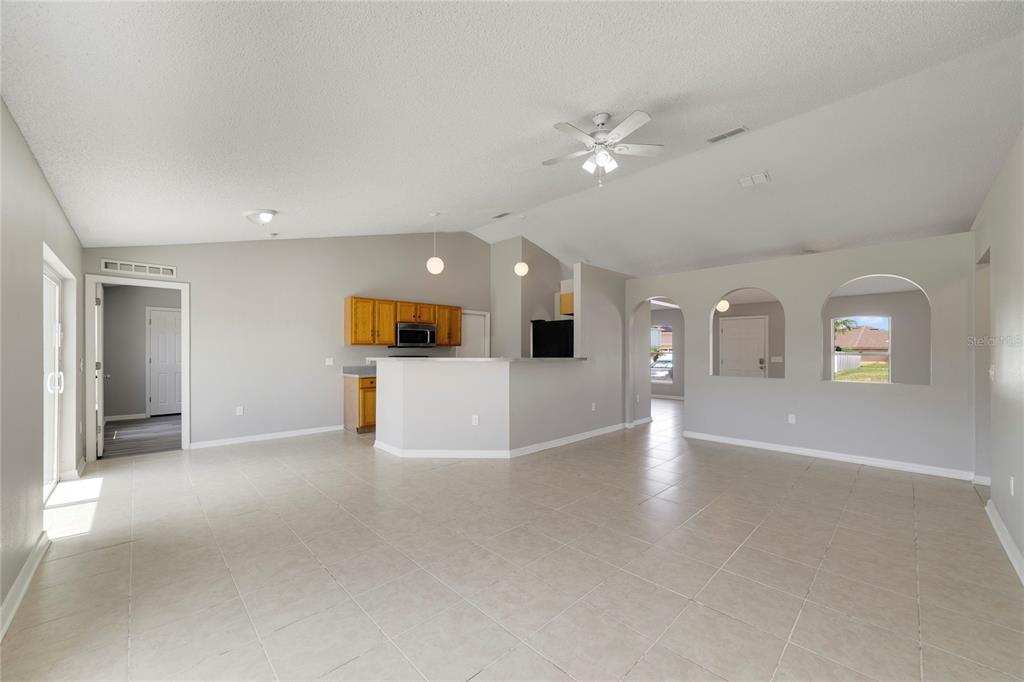 An open-concept living area features light tile flooring, a kitchen with wood cabinets, and arched doorways — 529 PEACE DRIVE, POINCIANA, FL