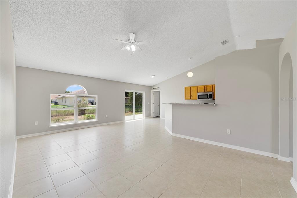 An open-concept living area features light tile flooring, a vaulted ceiling, and a kitchen pass-through — 529 PEACE DRIVE, POINCIANA, FL