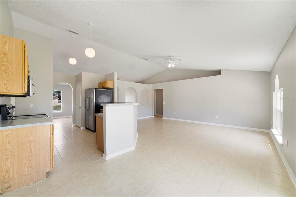 An open-concept kitchen and living area with light tile flooring and vaulted ceilings — 529 PEACE DRIVE, POINCIANA, FL