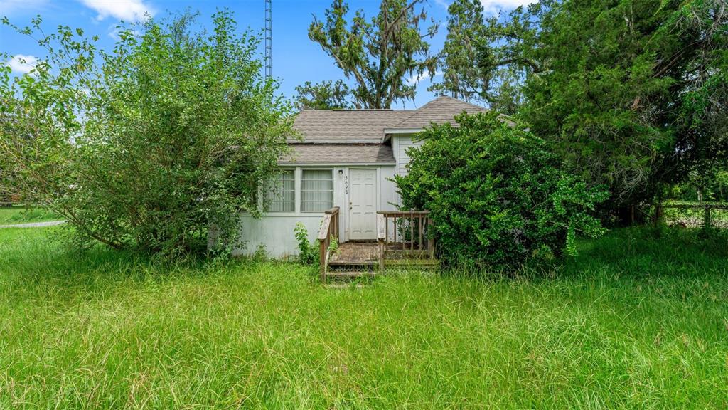 A small, white, single-story house with a wooden porch sits in a tall, grassy yard — 5698 NAVARRE AVENUE, HAMPTON, FL