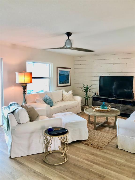A living room features white slipcovered furniture, a shiplap accent wall, and a ceiling fan — 7 DUNOON PLACE UNIT 203, DUNEDIN, FL