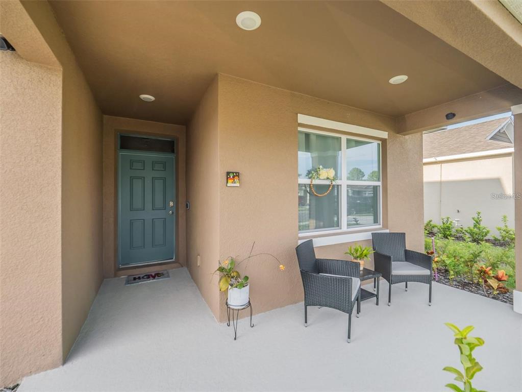 A covered front porch features a teal door, two chairs, and a small side table — 4885 PANGA AVENUE, MOUNT DORA, FL