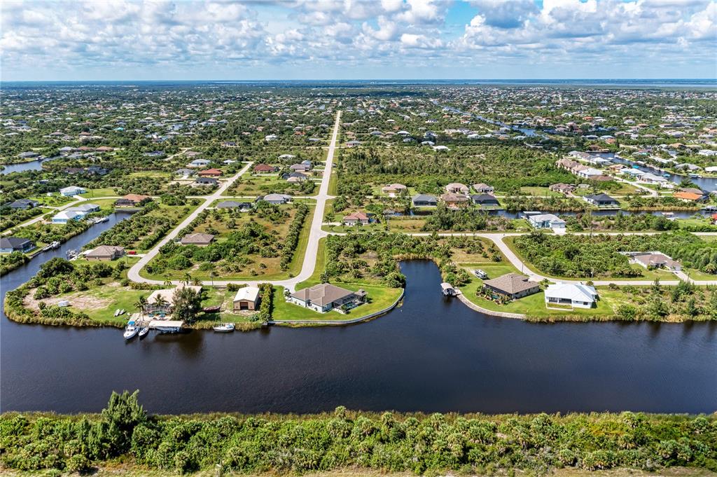 An aerial view shows houses along a canal in a suburban neighborhood with vegetation — 10453 POUGHKEEPSIE CIRCLE, PORT CHARLOTTE, FL