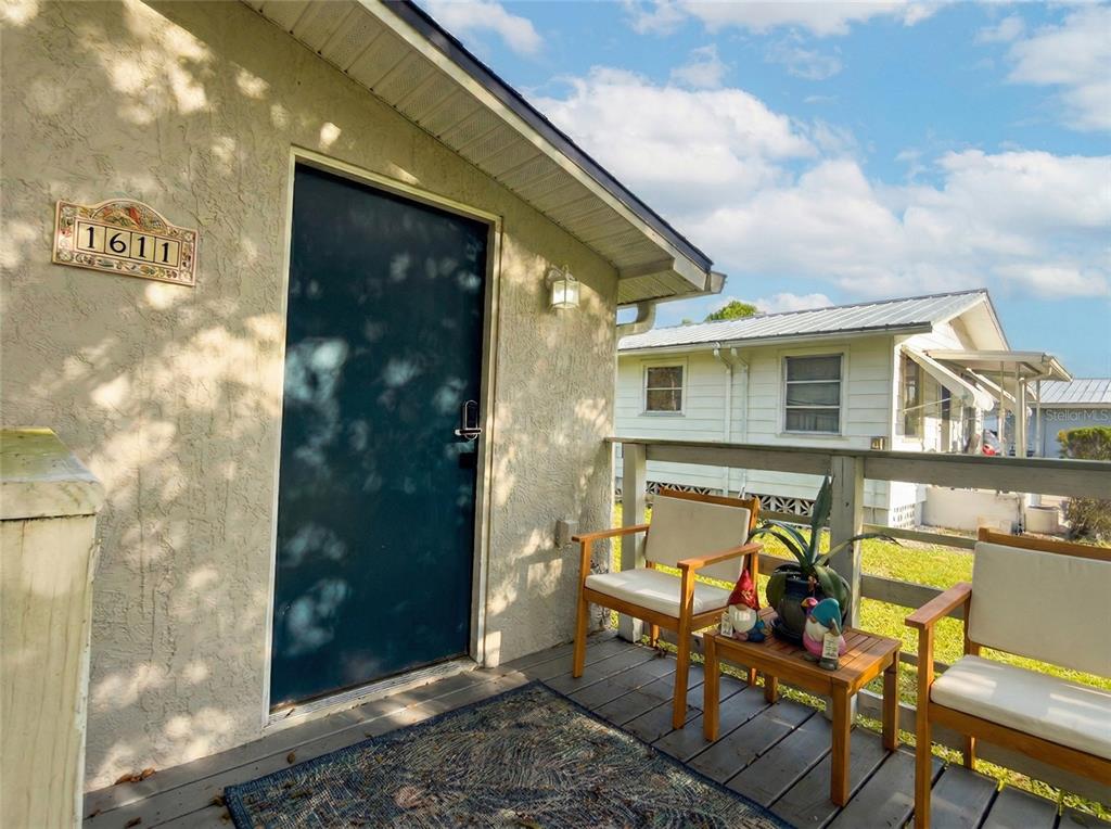 A wooden porch features two chairs, a small table with garden gnomes, and a dark door — 1611 SALMON STREET, ST CLOUD, FL