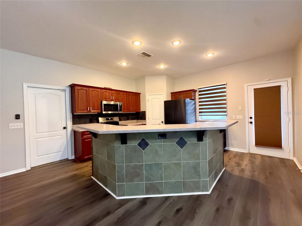 A kitchen features a tiled island, dark wood cabinets, stainless steel appliances, and wood-look flooring — 219 WILLOW BEND PARKWAY, LUTZ, FL