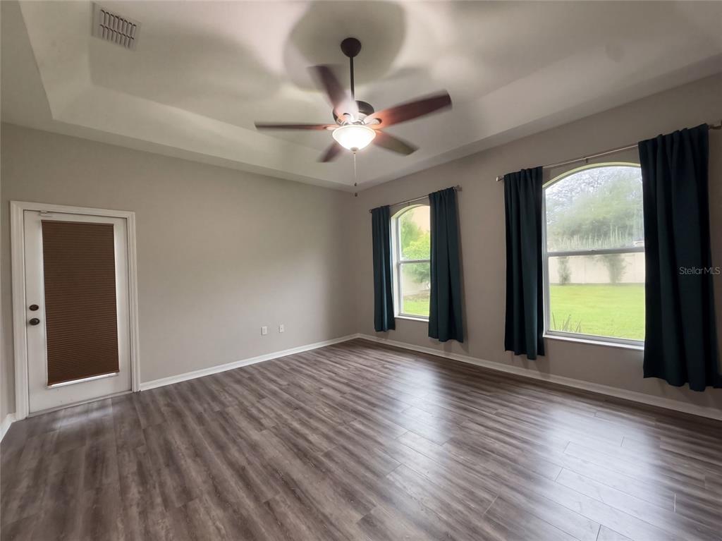 An empty room features wood-look flooring, a tray ceiling with a fan, and two arched windows — 219 WILLOW BEND PARKWAY, LUTZ, FL