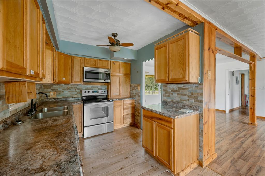 A kitchen features light wood cabinets, stainless steel appliances, stone backsplash, and wood-look flooring — 1619 N DOVER ROAD, DOVER, FL