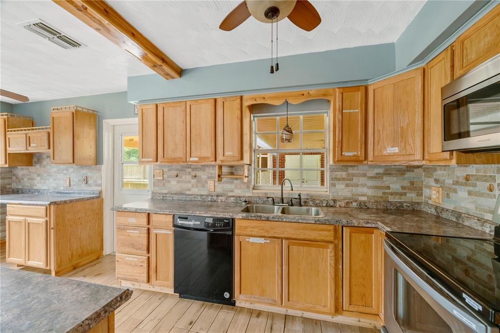 A kitchen features wood cabinets, a stone backsplash, laminate countertops, and a black dishwasher — 1619 N DOVER ROAD, DOVER, FL