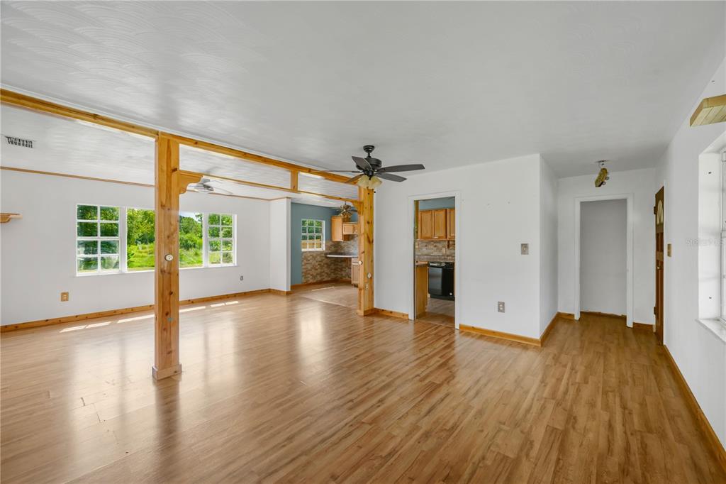 A living room with wood-look flooring, a wooden support beam, and an adjacent kitchen area — 1619 N DOVER ROAD, DOVER, FL