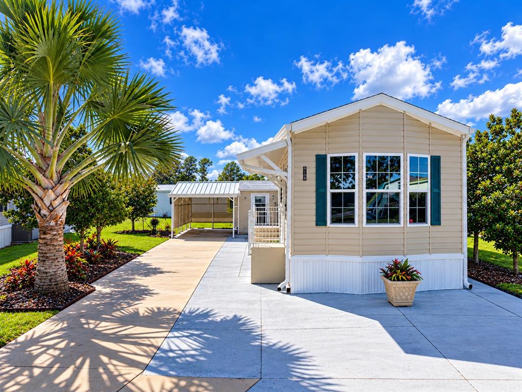 A tan manufactured home with a carport and palm tree under a blue sky — 5049 SHORE LINE DRIVE, POLK CITY, FL