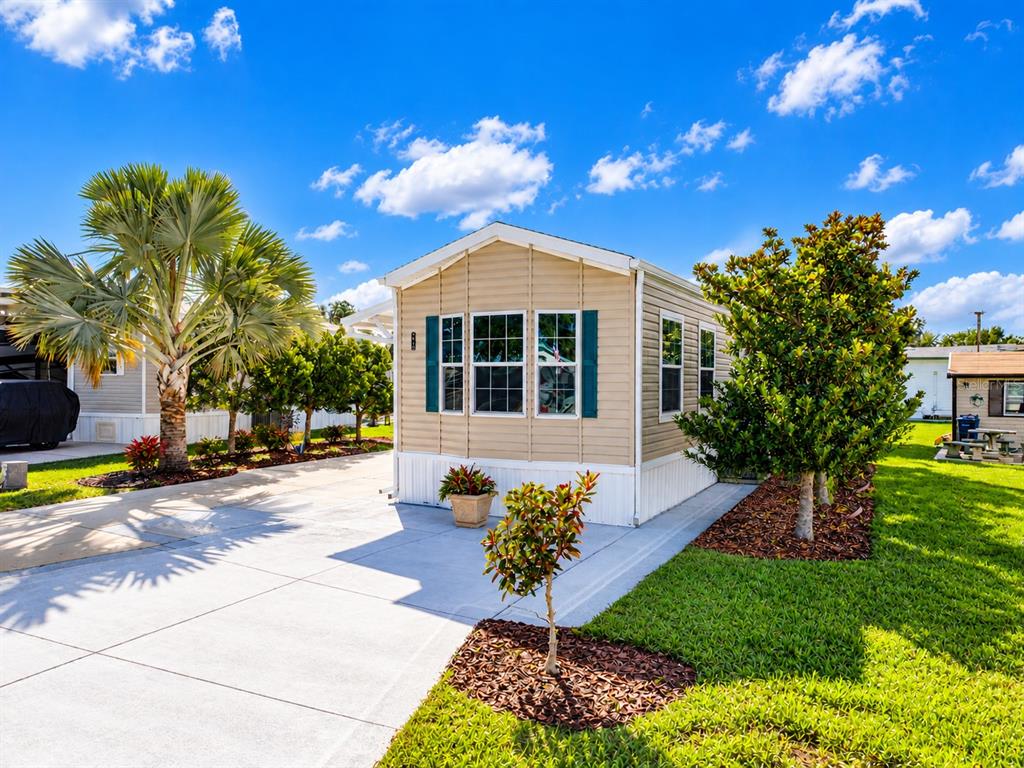 A tan manufactured home with dark shutters sits on a concrete driveway under a blue sky — 5049 SHORE LINE DRIVE, POLK CITY, FL