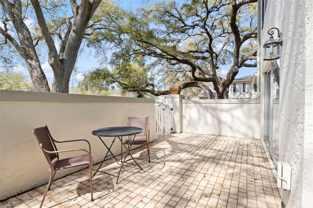 A paved patio features a small table, two chairs, and a white gate under trees — 6305 MORNINGMIST COURT UNIT 6305, TEMPLE TERRACE, FL