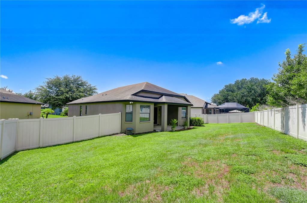 The backyard features a tan house with a covered patio and a white vinyl fence — 826 VINO VERDE CIRCLE, BRANDON, FL