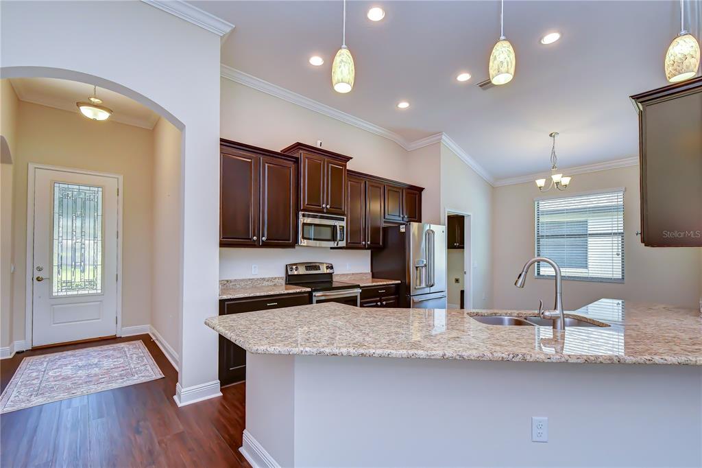 A kitchen features dark wood cabinets, granite countertops, a stainless steel refrigerator, and pendant lighting — 826 VINO VERDE CIRCLE, BRANDON, FL