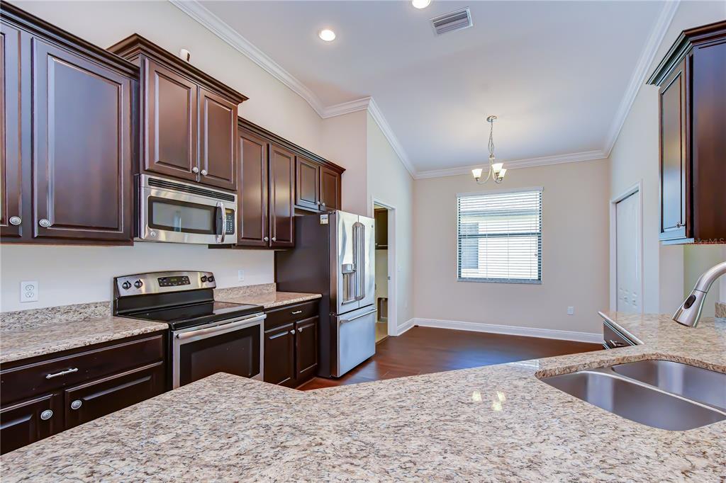 A kitchen features dark wood cabinets, granite countertops, stainless steel appliances, and an adjacent dining area — 826 VINO VERDE CIRCLE, BRANDON, FL