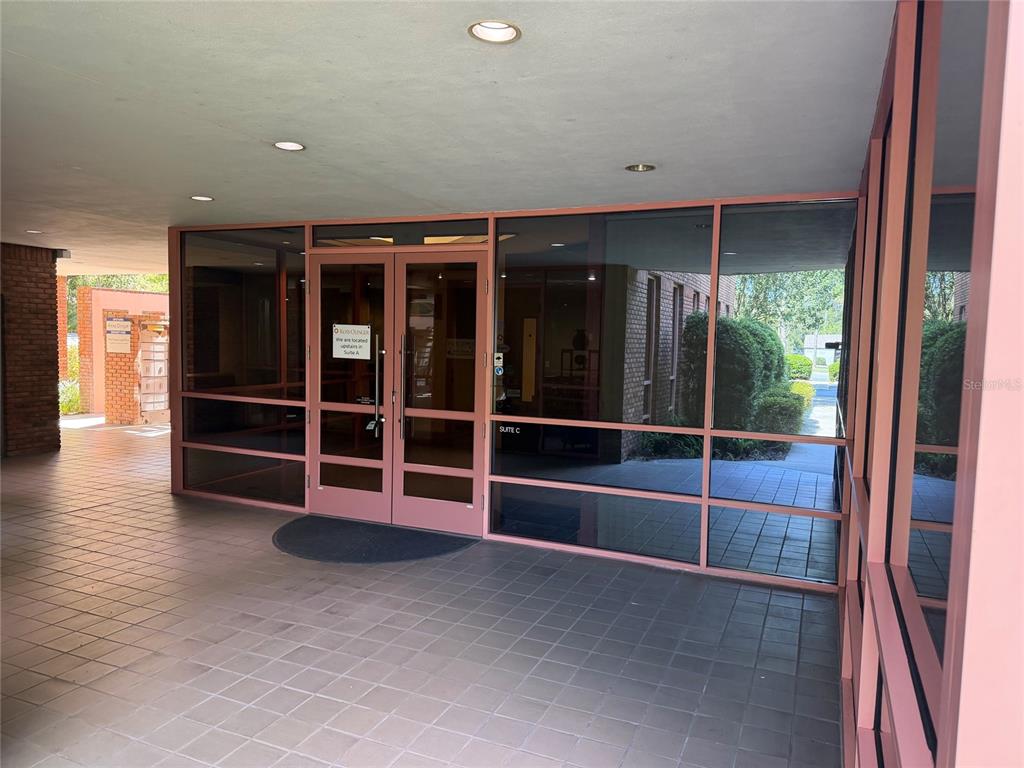 A covered outdoor walkway leads to a glass-fronted office entrance labeled Suite C — 2700 NW 43RD STREET UNIT C, GAINESVILLE, FL