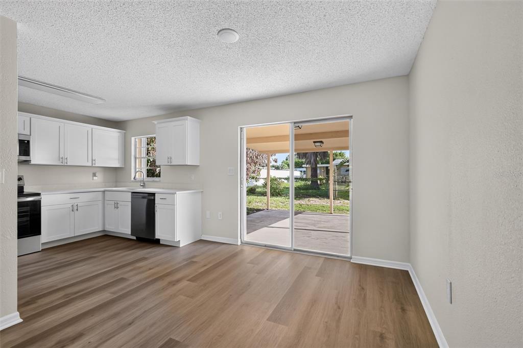A kitchen with white cabinets and wood-look flooring opens to a patio through sliding doors — 1856 JACKSON AVENUE, MELBOURNE, FL