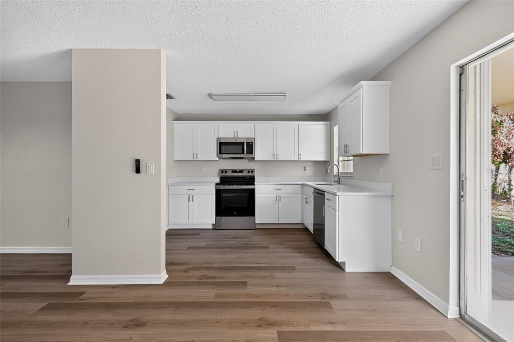 A kitchen with white cabinets, stainless steel appliances, and wood-look flooring — 1856 JACKSON AVENUE, MELBOURNE, FL