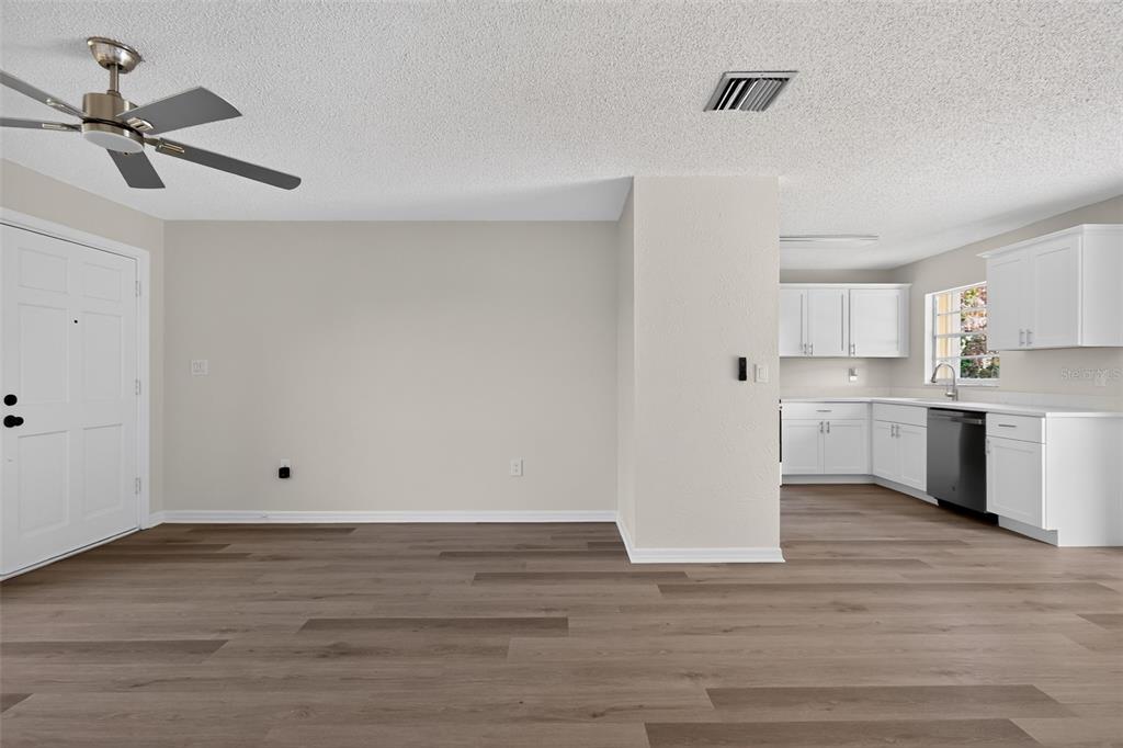 An open-concept living area with wood-look flooring leads into a kitchen with white cabinets — 1856 JACKSON AVENUE, MELBOURNE, FL