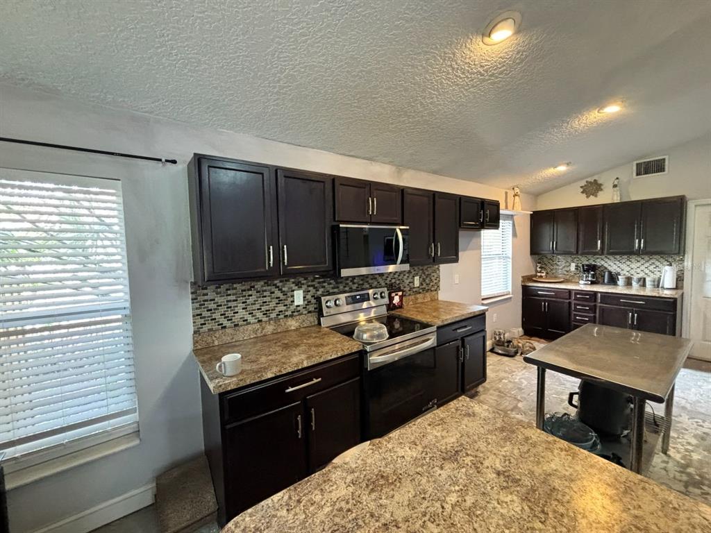 A kitchen features dark wood cabinets, granite countertops, stainless steel appliances, and a metal island — 6473 LONG BREEZE ROAD, ORLANDO, FL