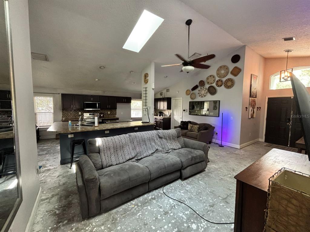 A living room with a gray sofa, kitchen island, and decorative wall baskets under a skylight — 6473 LONG BREEZE ROAD, ORLANDO, FL
