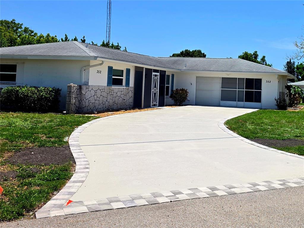 A single-story house features a white exterior, a stone accent wall, and a paved driveway — 352 PINE TREE ROAD, VENICE, FL