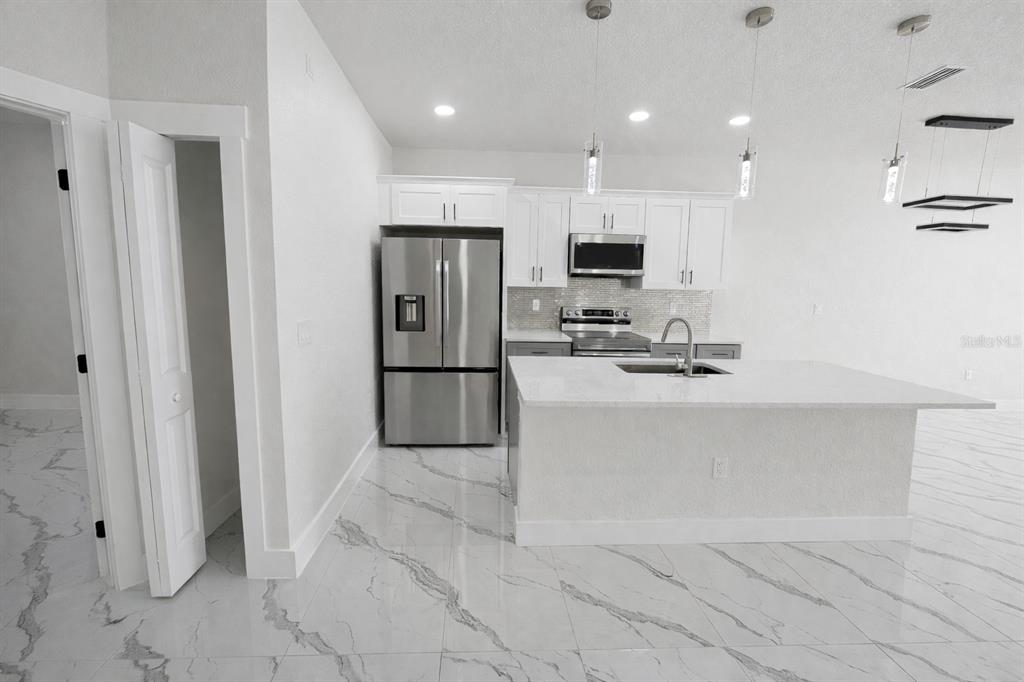 A modern kitchen features white cabinetry, stainless steel appliances, a center island, and marble-patterned flooring — 4820 24TH STREET SW, LEHIGH ACRES, FL