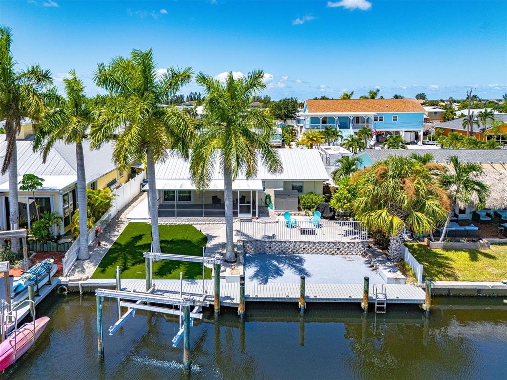 An aerial view shows a waterfront house with a boat lift, dock, and palm trees — 12262 BOAT SHELL DR, MATLACHA ISLES, FL