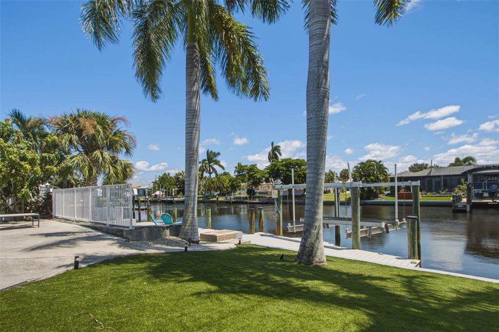 A backyard with artificial turf, palm trees, a white fence, and a private boat dock — 12262 BOAT SHELL DR, MATLACHA ISLES, FL
