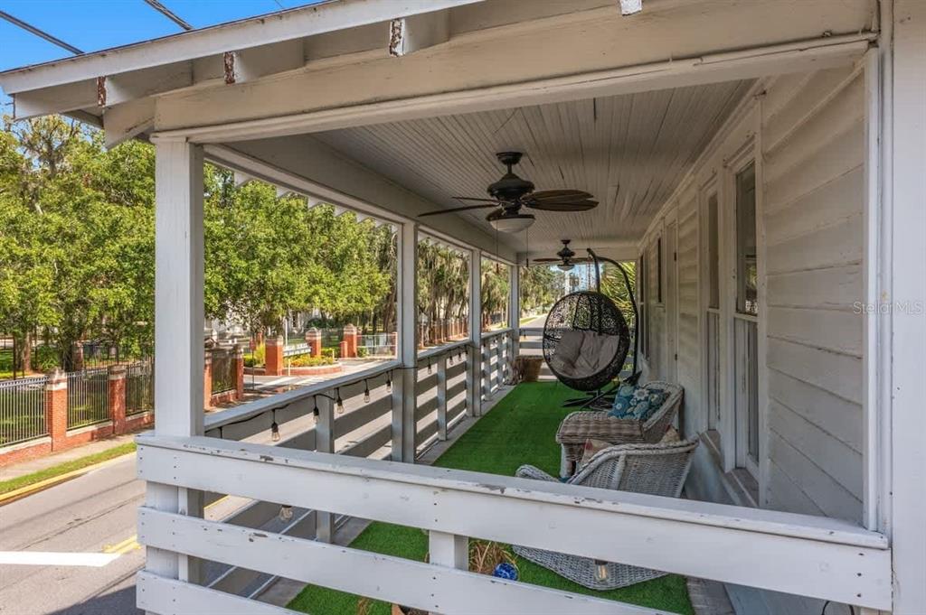 A covered porch features white railings, a ceiling fan, wicker furniture, and green turf flooring — 218 SAN MARCO AVENUE, ST AUGUSTINE, FL