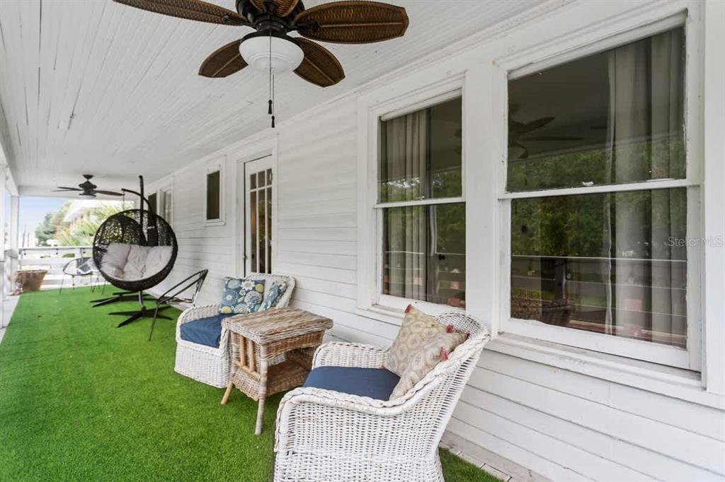 A covered porch features white siding, green artificial turf, wicker furniture, and a ceiling fan — 218 SAN MARCO AVENUE, ST AUGUSTINE, FL