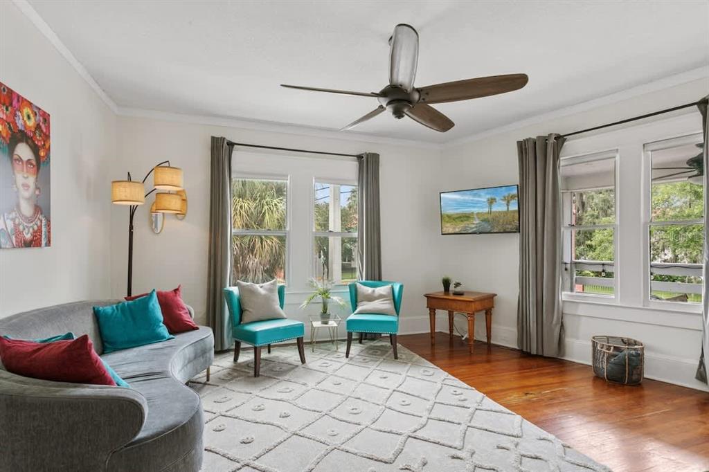 A living room features a curved sofa, two teal chairs, hardwood floors, and a ceiling fan — 218 SAN MARCO AVENUE, ST AUGUSTINE, FL
