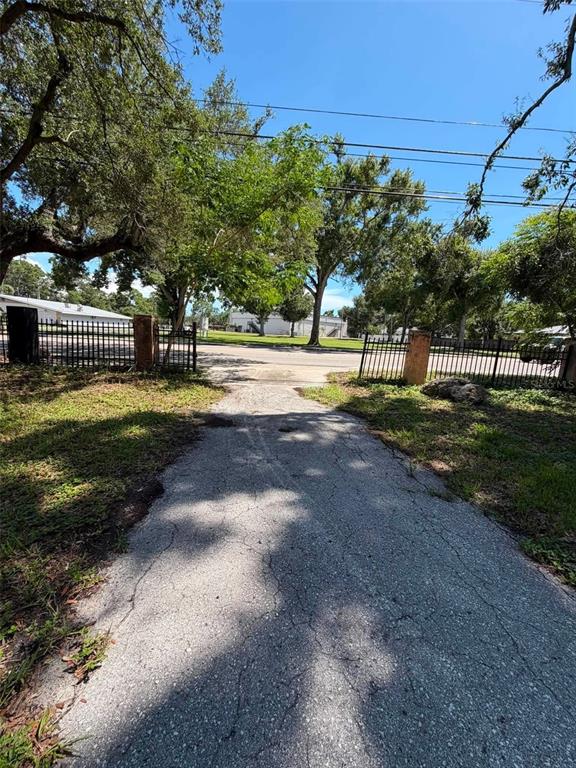 A paved driveway leads to an open gate with a metal fence and mature trees — 4365 78TH AVENUE N, PINELLAS PARK, FL