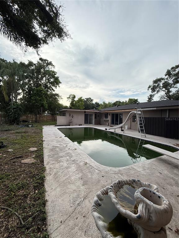 A backyard features a green swimming pool with a slide and a wooden privacy fence — 384 LENTZ ROAD, BELLEAIR BLUFFS, FL